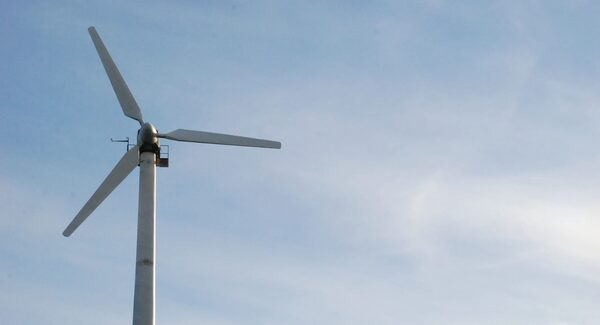 A small white wind turbine on a tall pole against a blue sky