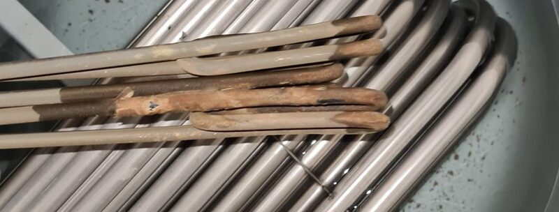 Close-up of limescale-covered immersion heater elements inside a hot water cylinder