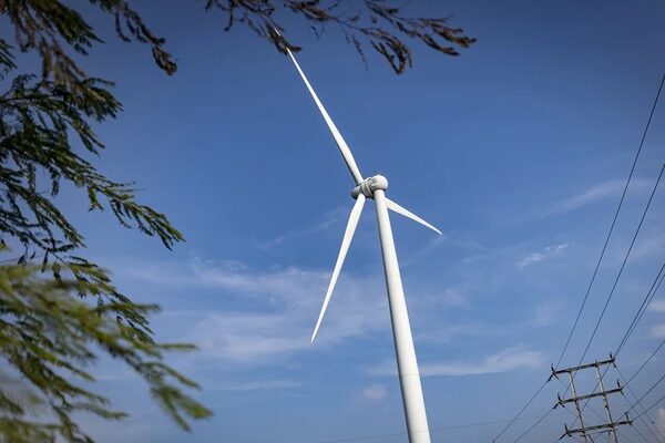 A white wind turbine against a blue sky with power lines and a transmission pylon in the background