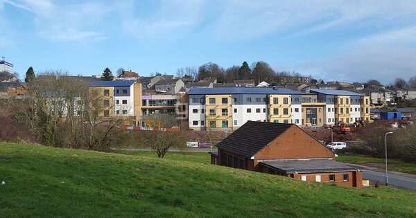 A new-build assisted living development with solar panels on its roofs, seen from a distance across a grassy slope in Newport, South Wales