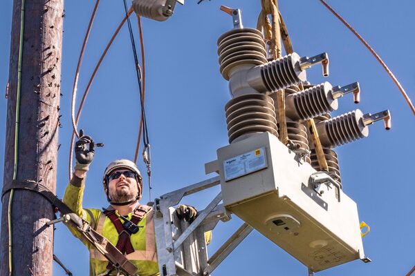 An electricity linesman in hi-vis and hard hat working on overhead power line equipment mounted on a wooden pole