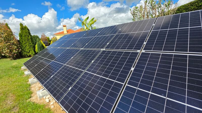 Ground-mounted solar panels in a garden with a house and trees behind