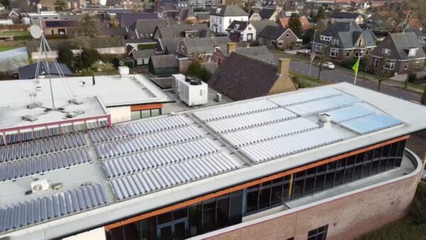 Aerial view of rows of solar thermal collector tubes installed on the flat roof of a building in a residential neighbourhood