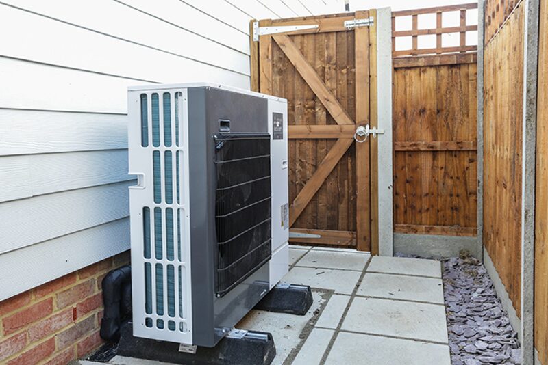 An air source heat pump unit installed outside a house beside a wooden garden gate