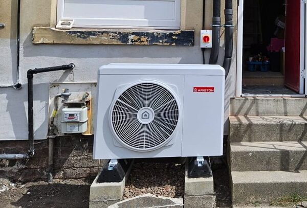 An Ariston air source heat pump installed outside a house next to a gas meter and steps