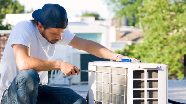A technician in a cap using a screwdriver to work on an outdoor air source heat pump unit