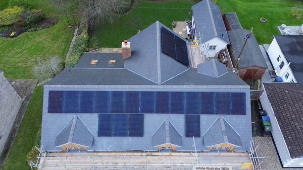 Aerial view of a large slate-roofed house with many solar panels installed on the roof and scaffolding at the front