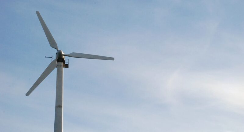 A small white wind turbine on a tall pole against a blue sky