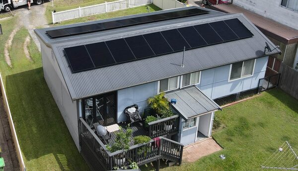 An aerial view of a single-storey house with a large array of black solar panels covering its metal roof