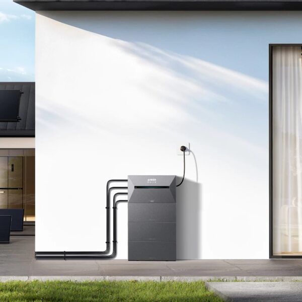 An Anker Solarbank home battery unit standing against an exterior house wall with cables running along the ground