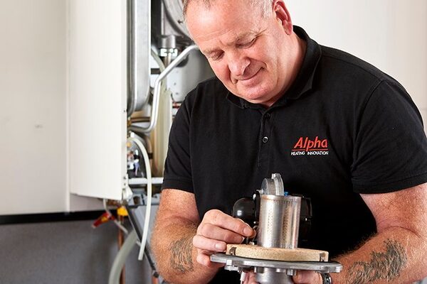 An Alpha Heating Innovation engineer servicing a boiler component in front of a wall-mounted boiler