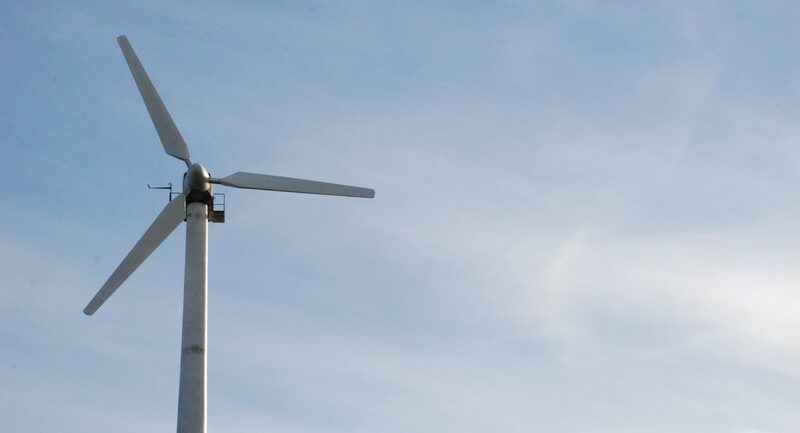 A small white wind turbine on a tall pole against a blue sky
