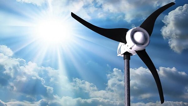A small white wind turbine with three black blades on a pole against a bright sunlit cloudy sky