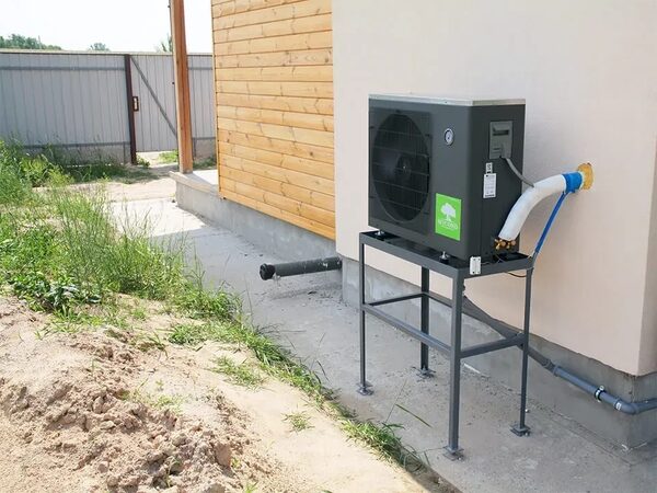A Mycond air source heat pump installed on a metal stand outside a house, connected to pipework through the wall