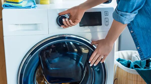 A woman turning the dial on a white washing machine in a home laundry setting