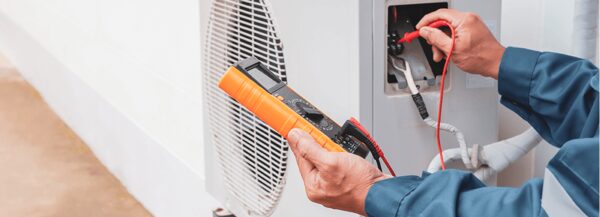 A technician using a multimeter to test an outdoor air conditioning or heat pump unit
