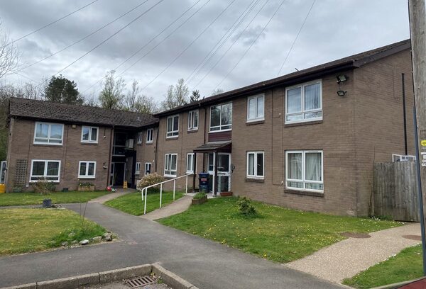 A brick-built social housing block of flats with lawns and a paved path under an overcast sky
