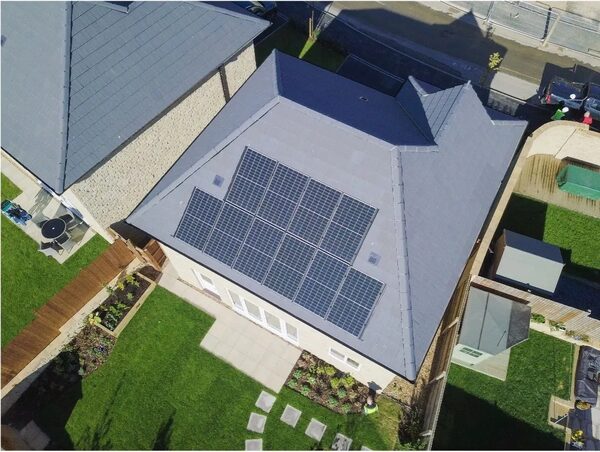 Aerial view of a grey-roofed house with a large array of solar panels on the roof and a garden below