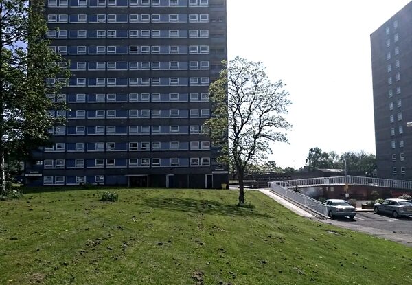 Tall residential tower blocks with grass and a car park in front, likely a UK housing estate