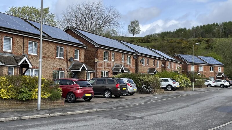 A row of brick terraced houses with solar panels on their roofs, cars parked along the street