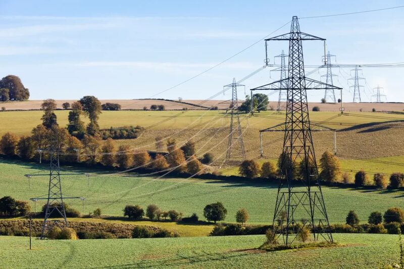 Electricity pylons and power lines crossing rolling green countryside fields