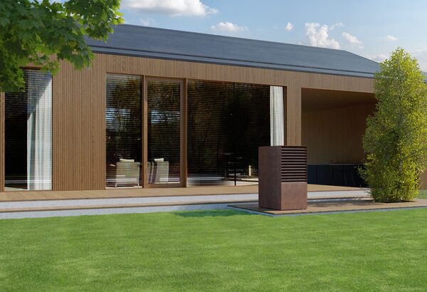 An outdoor air-source heat pump unit installed on a patio beside a modern timber-clad house with a lawn
