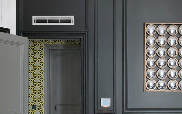 A white ventilation grille installed high on a dark grey panelled interior wall above a doorway