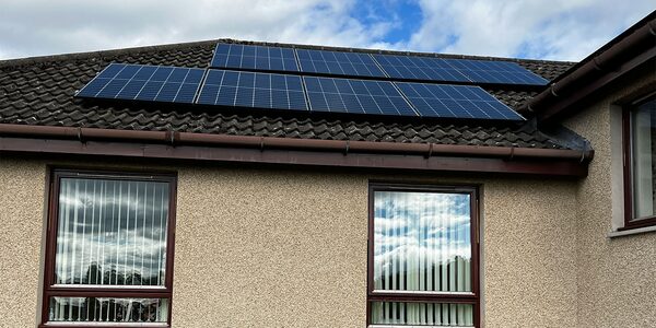Solar panels installed on the tiled roof of a rendered house with two windows below