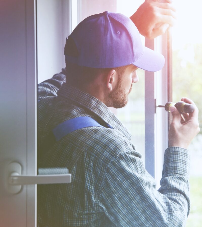 A workman in a cap using a screwdriver to fit or adjust a uPVC window or door frame