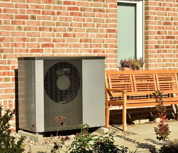 An air source heat pump unit installed outside a red brick house next to a wooden garden bench