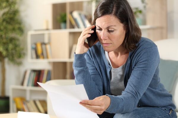 A woman at home on a mobile phone reading a paper letter or bill