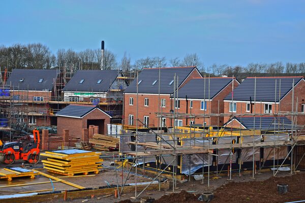 A UK housing development site with new brick houses under construction, scaffolding and a small orange roller