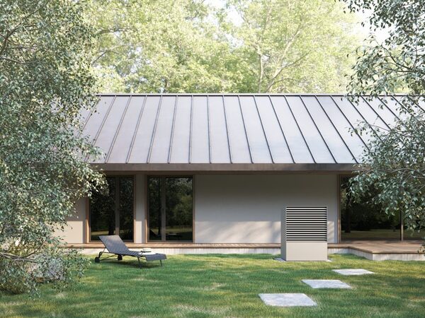 A heat pump outdoor unit installed beside a modern single-storey house with a metal roof and lawn
