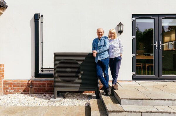 A couple standing beside an Aira air source heat pump installed outside their house