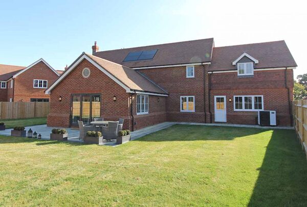 A new brick eco-home with solar panels on the roof, an air source heat pump unit at the side, and a large lawn garden