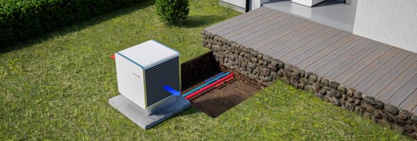 A Heliotherm air-source heat pump outdoor unit on a concrete slab beside a house, with buried pipework shown in a cutaway