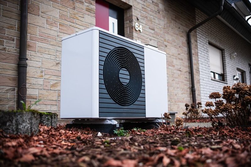 An air source heat pump unit installed outside a brick house beside the front door