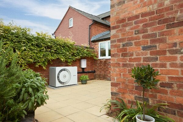 An air source heat pump unit installed on a paved patio beside a red brick house wall