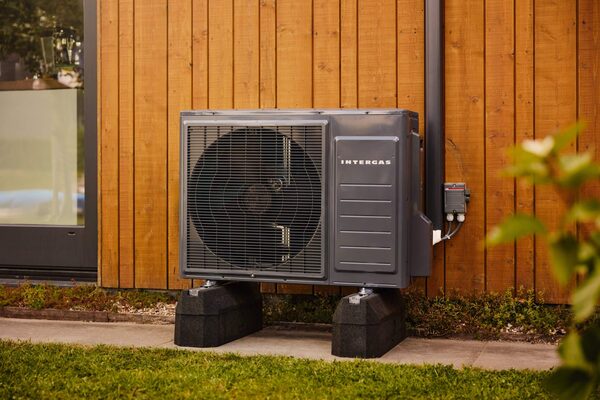 An Intergas air source heat pump unit installed outside a timber-clad house on plastic feet beside a lawn