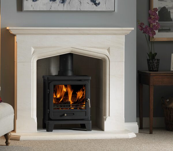 A black wood-burning stove with flames burning inside, installed in a cream stone fireplace in a living room