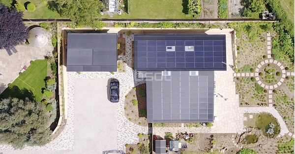 Aerial view of a house with a large rooftop solar panel array, a car on the driveway and gardens