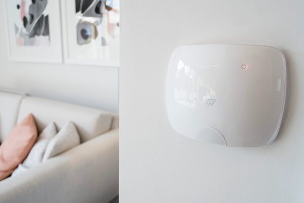 A white Wondrwall smart home control panel mounted on a wall in a bright living room with a sofa and framed art
