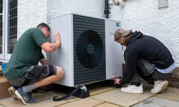 Two installers positioning an air source heat pump unit outside a house