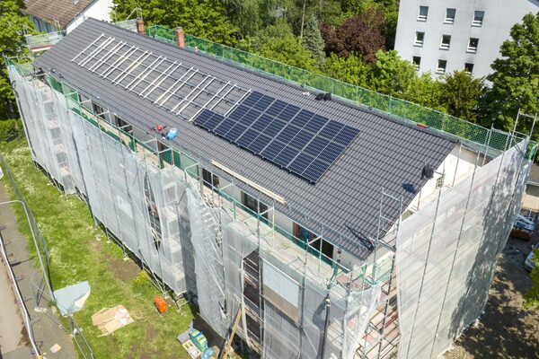 Aerial view of a house wrapped in scaffolding and sheeting with solar panels being installed on its tiled roof