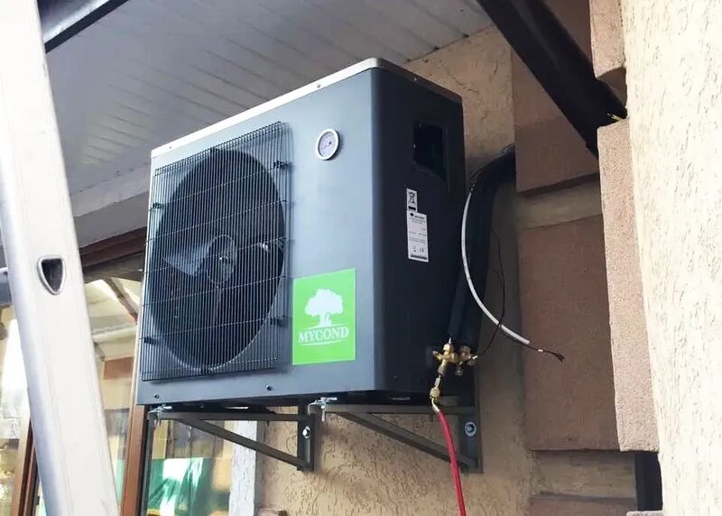 A Mycond air source heat pump unit mounted on an exterior house wall with visible pipework