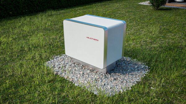 A white Heliotherm ground-source heat pump outdoor unit installed on a gravel bed in a grassy garden