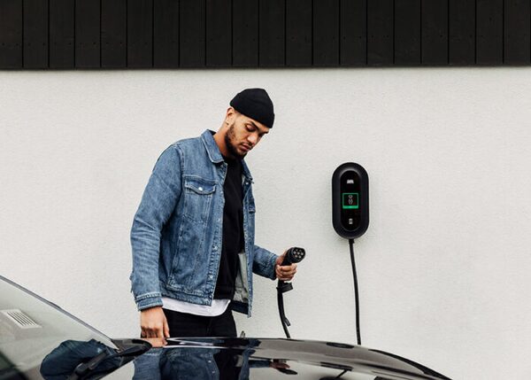 A man plugging a charging cable into an electric car next to a wall-mounted EV chargepoint on a white wall