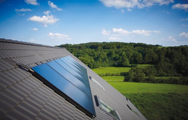 Flat-plate solar thermal panels mounted on a tiled roof overlooking green countryside