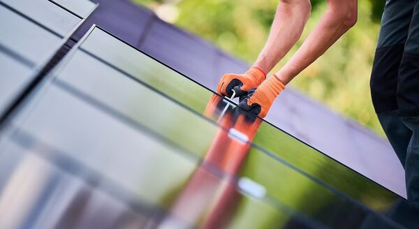 A gloved installer fitting a solar panel on a roof