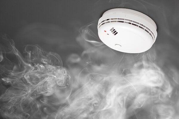 A white ceiling-mounted smoke alarm surrounded by swirling smoke
